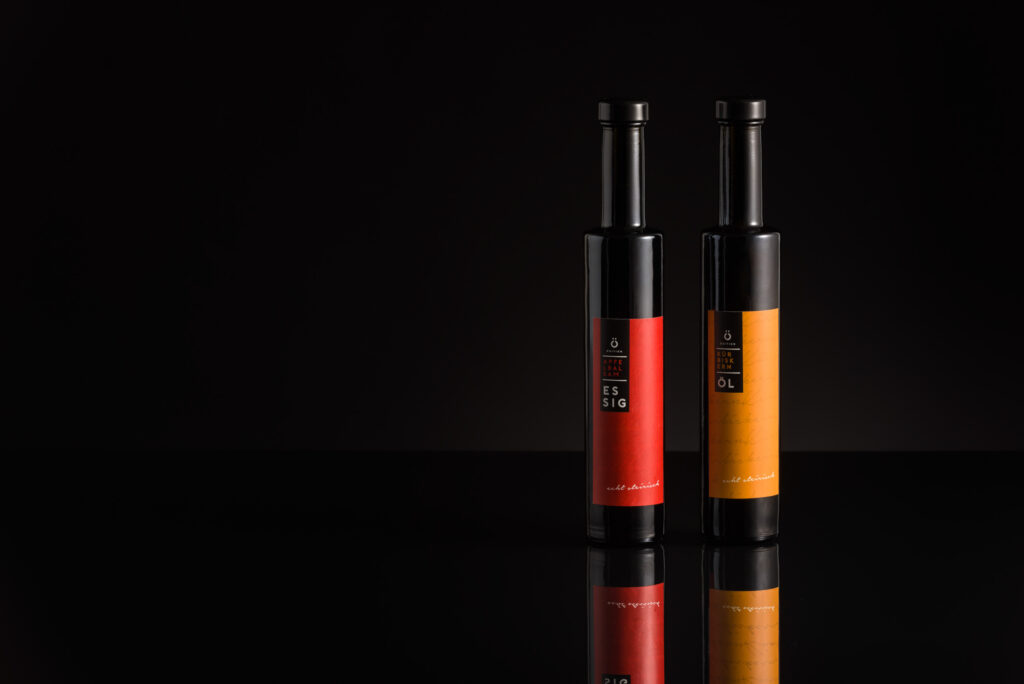 Produktfotografie Essig und Öl im Fotostudio für Genuss am See - schwarzer Hintergrund, schwarze Flaschen mit roten und orangen Etiketten