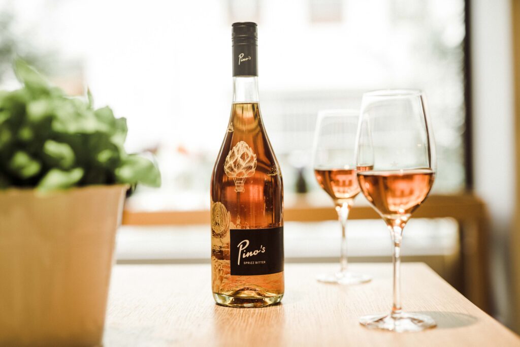 Werbefotografie für das Getränk "Pino's" - Produktaufnahme der Flasche mit zwei Gläsern auf einem Tisch