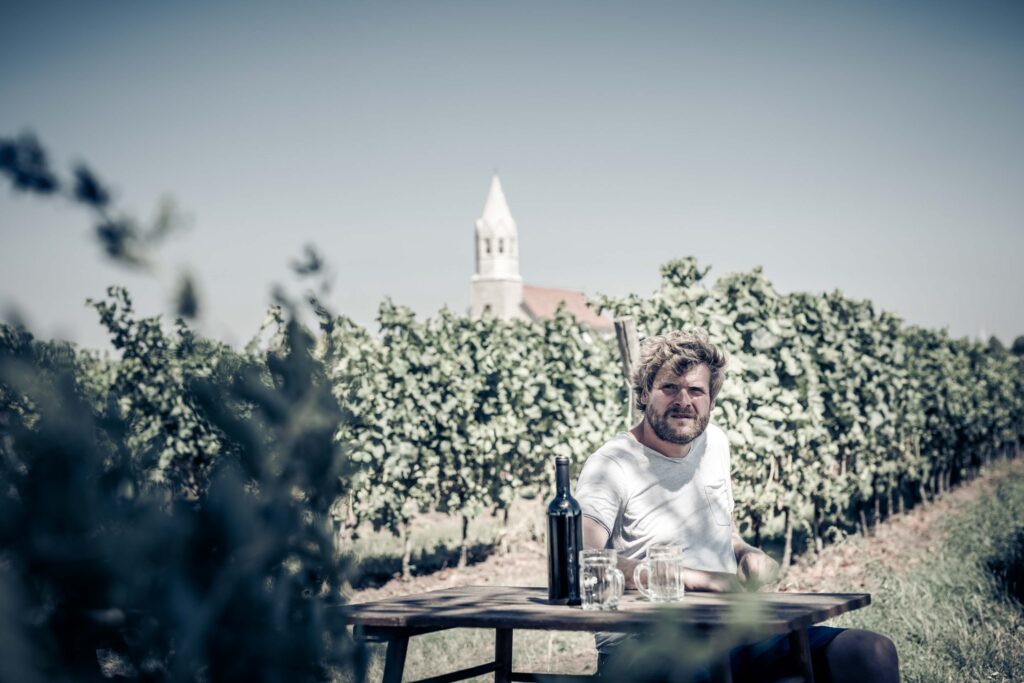 Werbefotografie- ein junger Mann sitzt an einem Tisch in seinem Weingarten