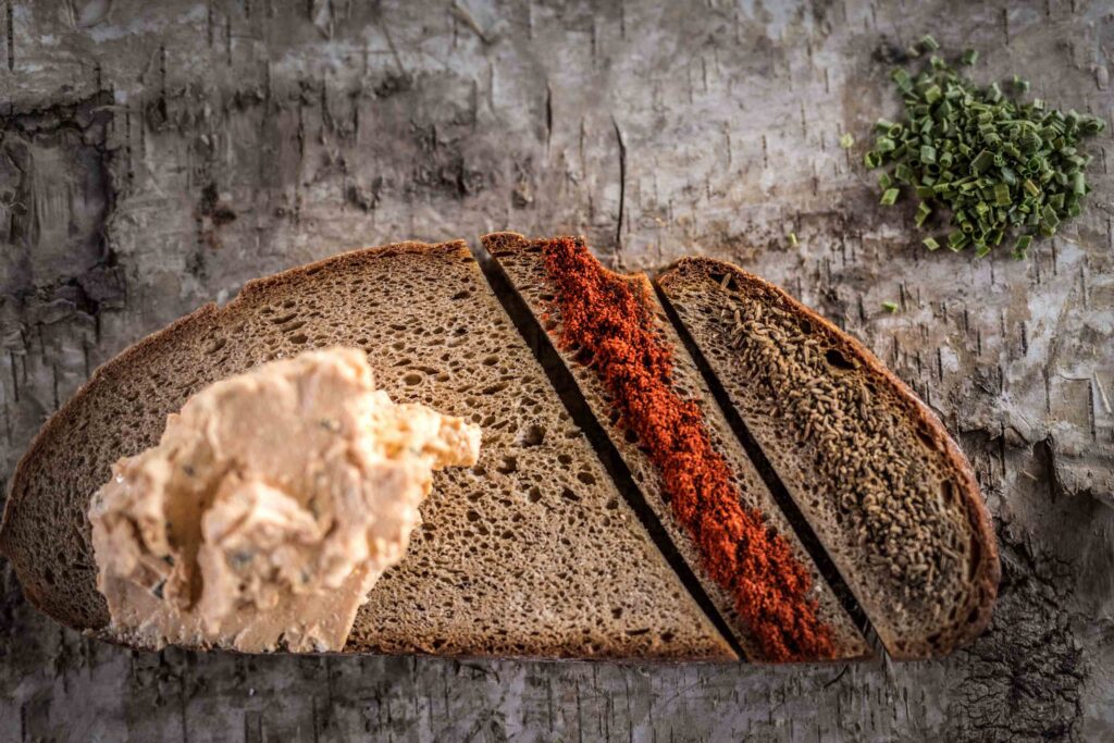 Foodfotografie eines Brotes - rechts sind zwei geometrische Streifen des Brotes abgeschnitten und mehrere Aufstriche sind auf dem Brot gestrichen