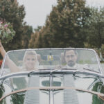Hochzeitsfotografie - junges Brautpaar fährt in einem Oldtimer