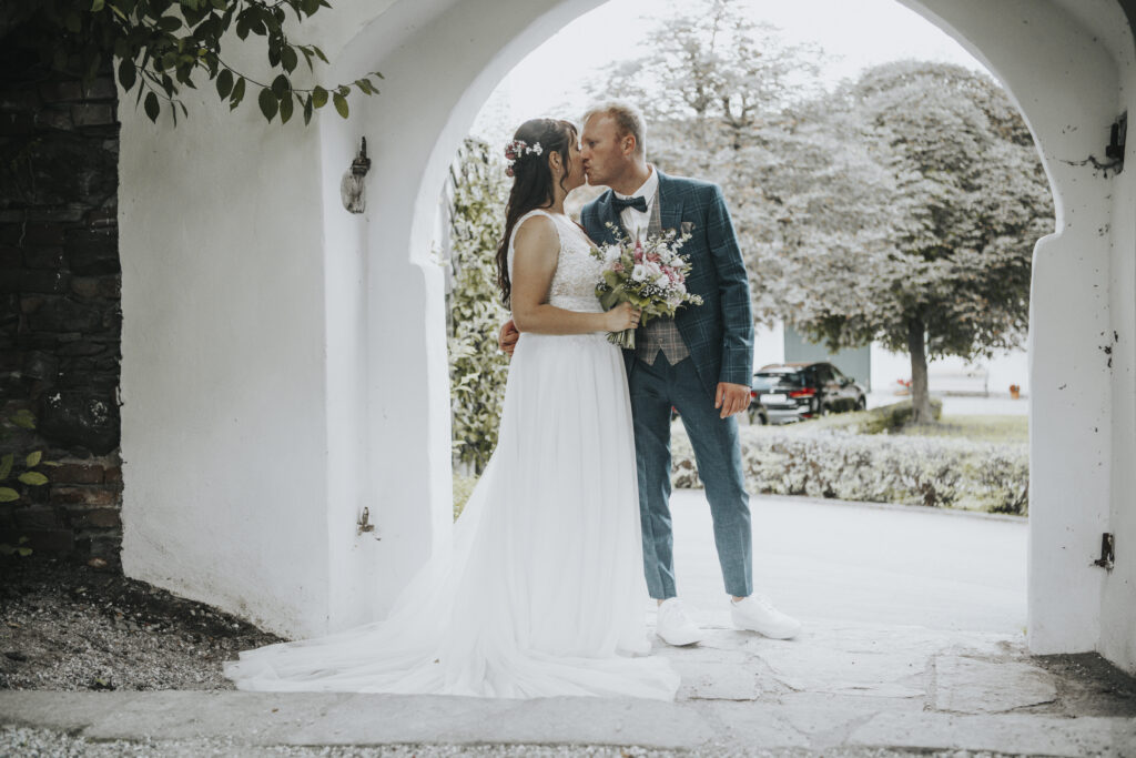 Hochzeitsfotografie- Porträtaufnahme eines Brautpaares, wie es sich unter einem Torbogen küsst
