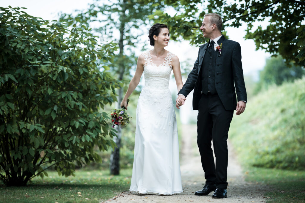 Hochzeitsfotografie - Porträtaufnahme eines Brautpaares beim Schlendern durch einen grünen Garten