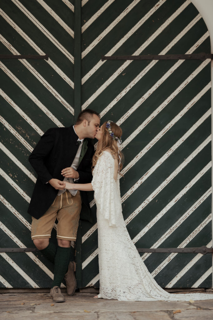 Hochzeitsfotografie- Porträtaufnahme eines Brautpaares vor einer grünen Holztür, sich küssend