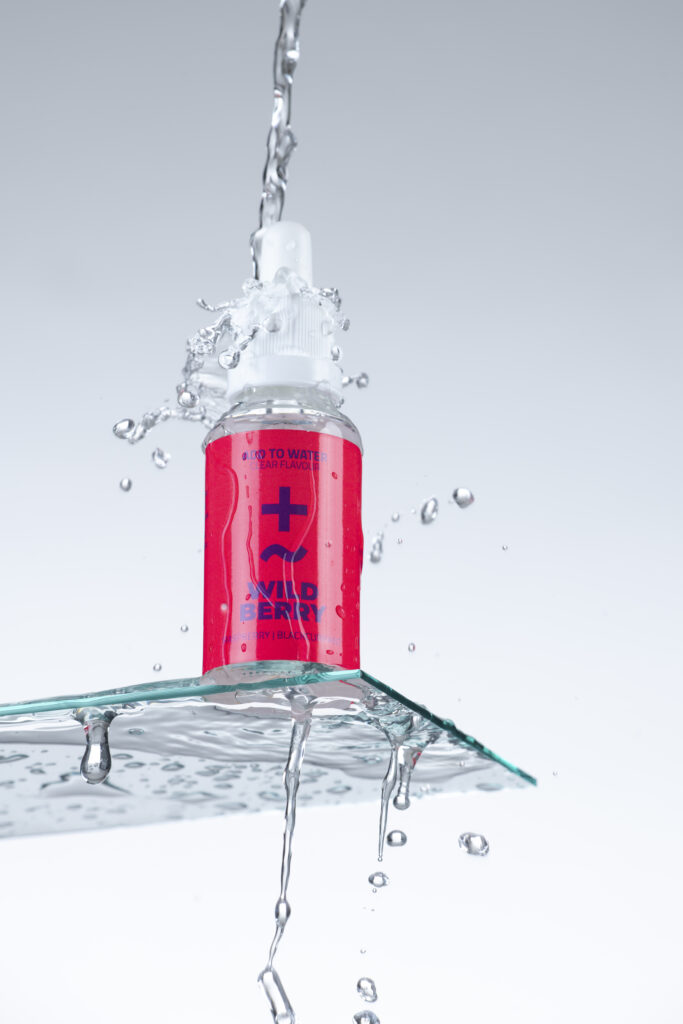 Produktfotografie- ein Fläschchen auf Glasfläche mit Wassertropfen & Wasserspritzer
