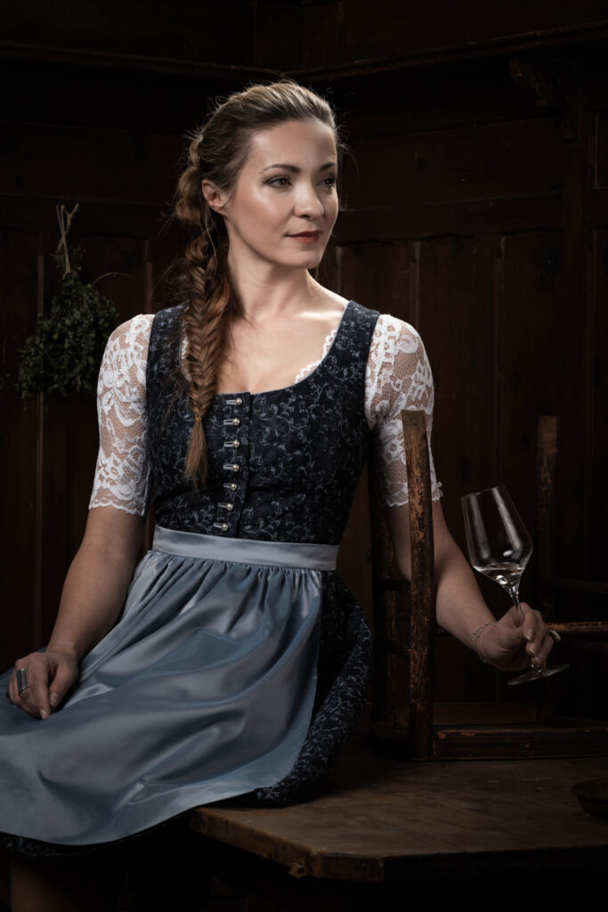 Portraitfotografie im Fotostudio - Porträt einer Frau an einem Tisch. Sie trägt Tracht und hält ein Glas Wein in ihrer Hand