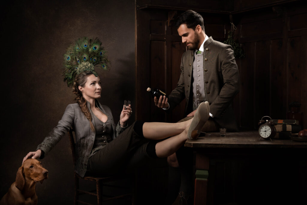 Portraitfotografie im Fotostudio - Porträt eines Mannes und einer Frau an einem Tisch. Beide sind in Tracht gekleidet, die Frau trägt einen Federhut