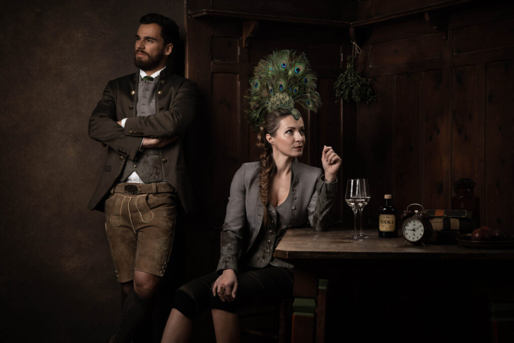 Portraitfotografie im Fotostudio - Porträt eines Mannes und einer Frau an einem Tisch. Beide sind in Tracht gekleidet, die Frau trägt einen Federhut