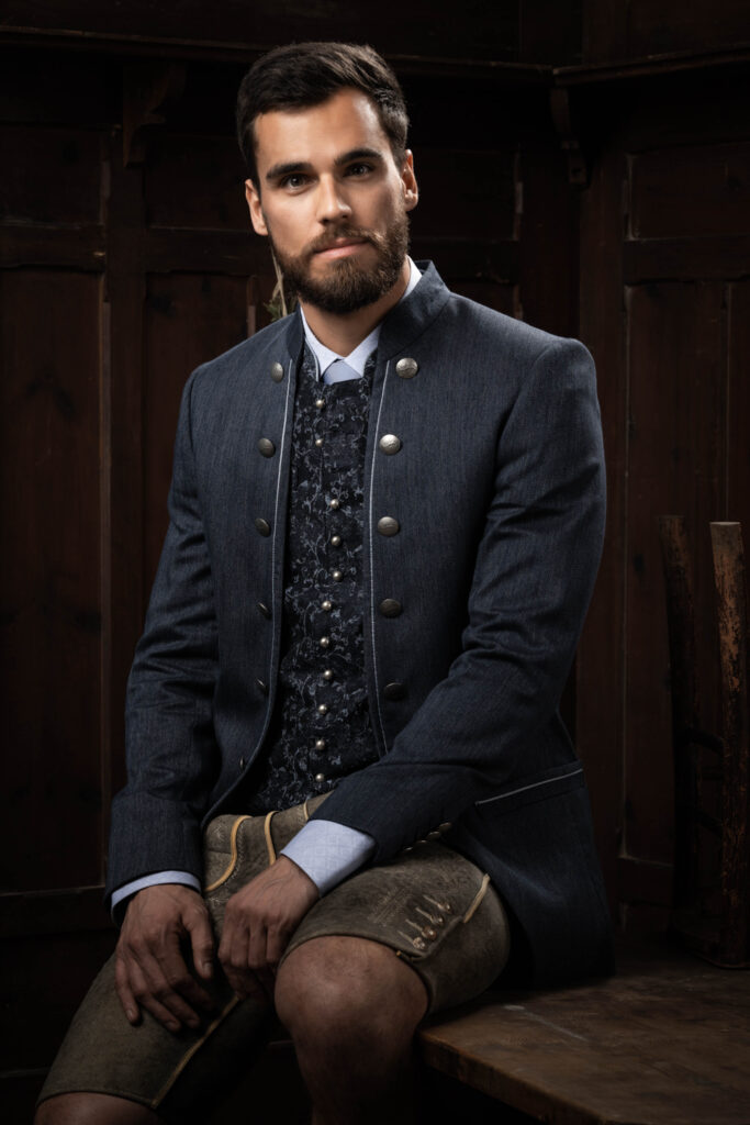 Portraitfotografie im Fotostudio - Porträt eines Mannes auf einem Tisch sitzend, in Tracht gekleidet