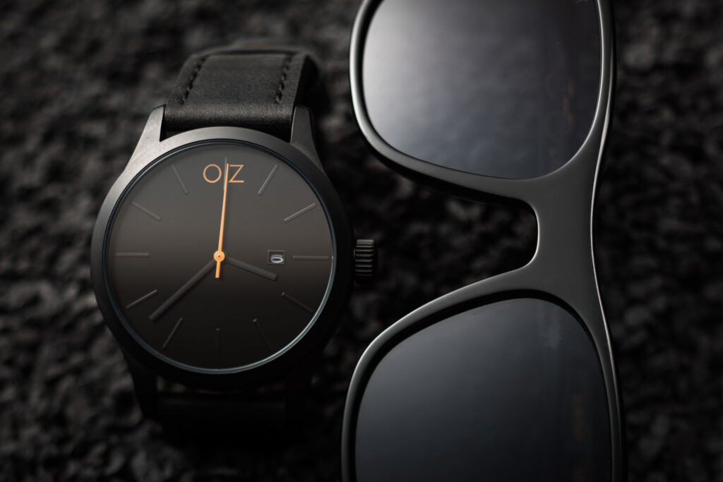 Produktfotografie Uhr von OZ und Brille von Lasnik - alles in schwarz nur die Logos auf den Produkten sind gold