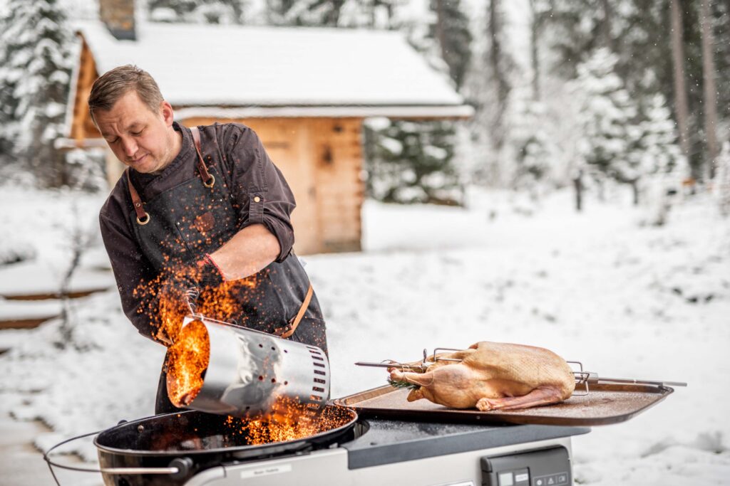 Werbefotografie für Genuss am See - Portraitaufnahme des Koches (Outdoor) bei der Zubereitung einer Gans mit einem Grill