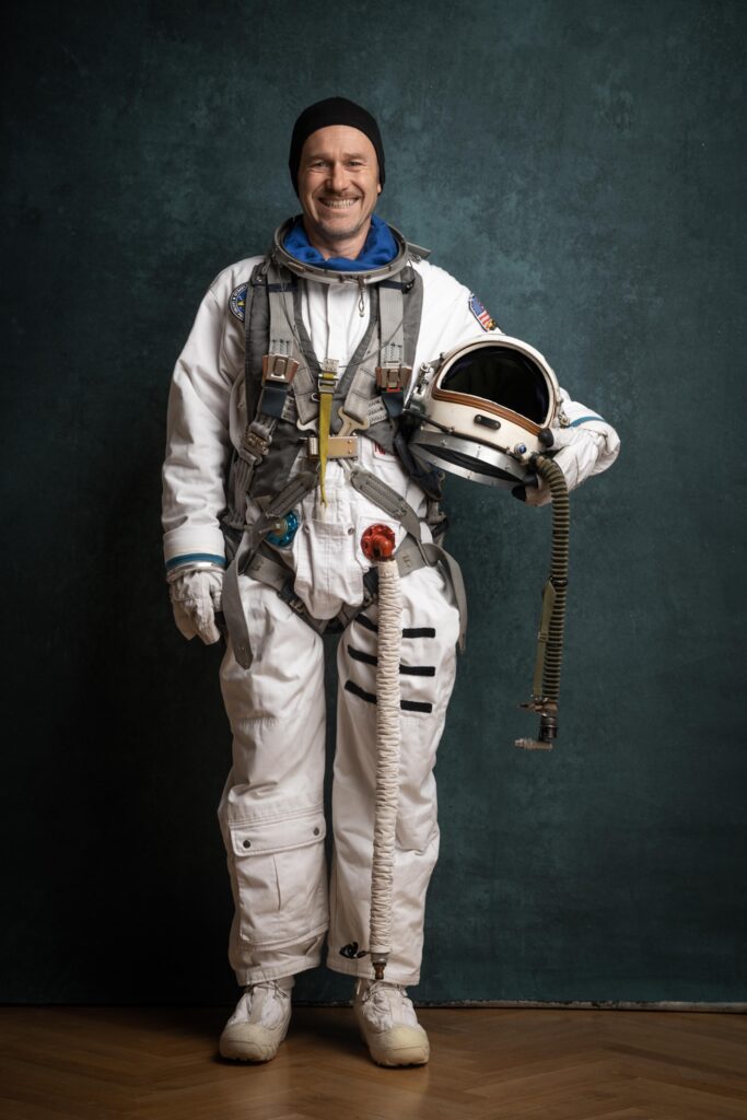 Portrait eines Mannes (Dieter Sajovic) im Astronautenkostüm vor blauem Hintergrund- Ein Ganzkörperfoto im Hochformat