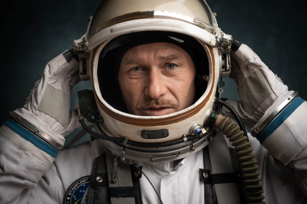 Portrait eines Mannes (Dieter Sajovic) im Astronautenkostüm vor blauem Hintergrund. Das Bild ist im Querformat