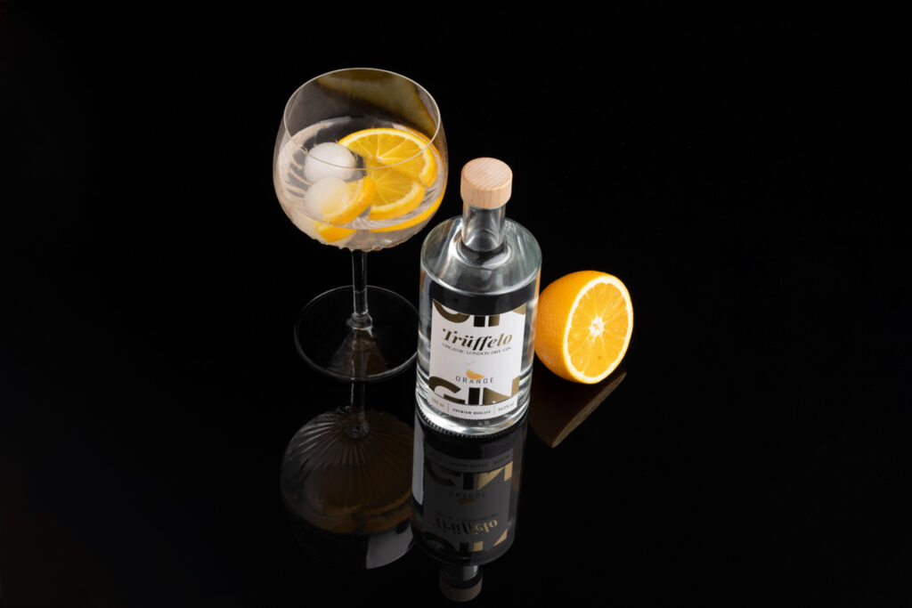 Produktfotografie für Trüffel - im Studio- schwarzer Hintergrund- eine Flasche Gin, ein großes Weinglas, gefüllt mit Eiswürfeln und Orangen