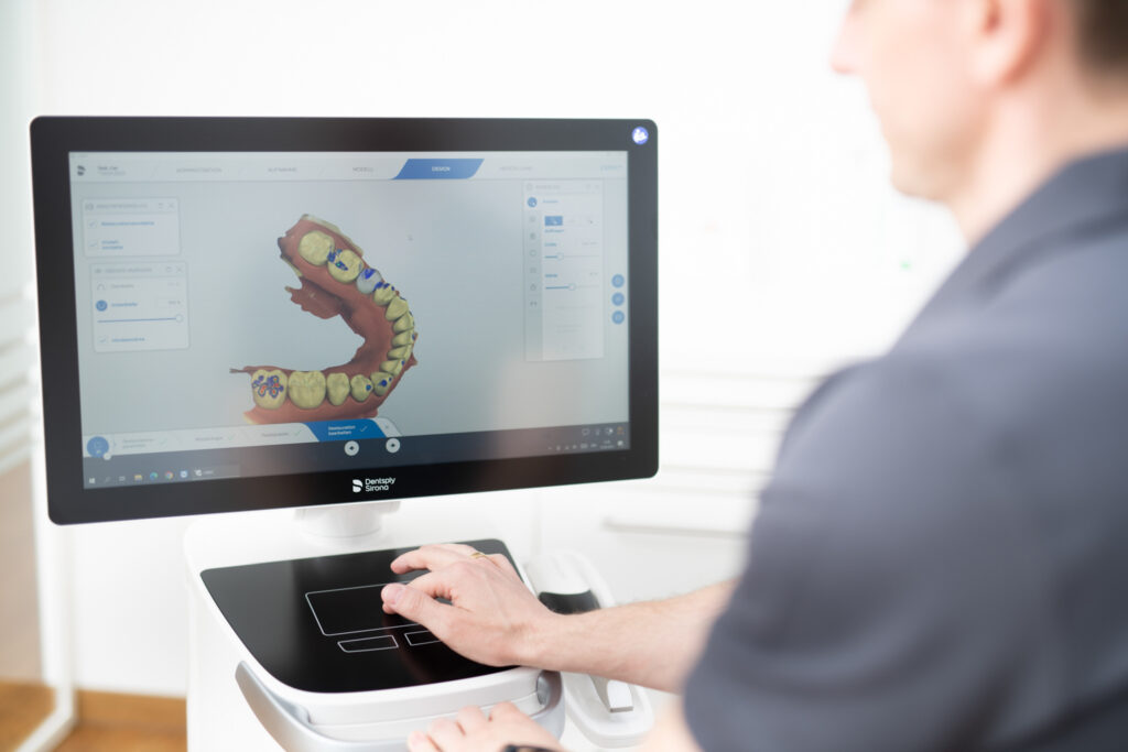 Ein Mann (Zahnarzt) sitz vor einem Bildschirm und schaut sie ein 3D Modell eines Gebisses an