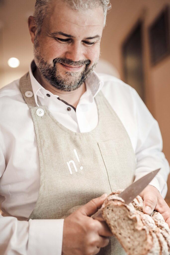 Portrait des Geschäftsführers von Vinum Novum wie er ein Brot aufschneidet