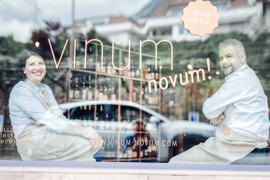Man sieht einen Mann und eine Frau durch eine Glasscheibe mit der Aufschrift "Vinum Novum"