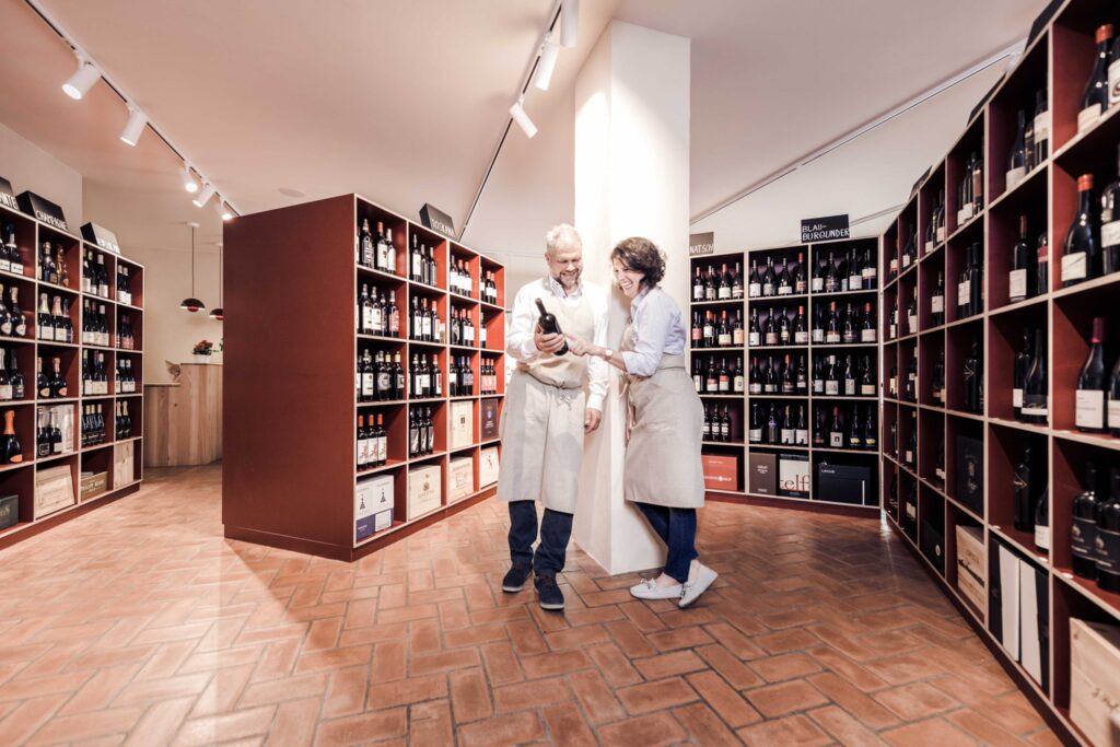 Die Geschäftsführer stehen zwischen den Weinregalen und besprechen einen Wein