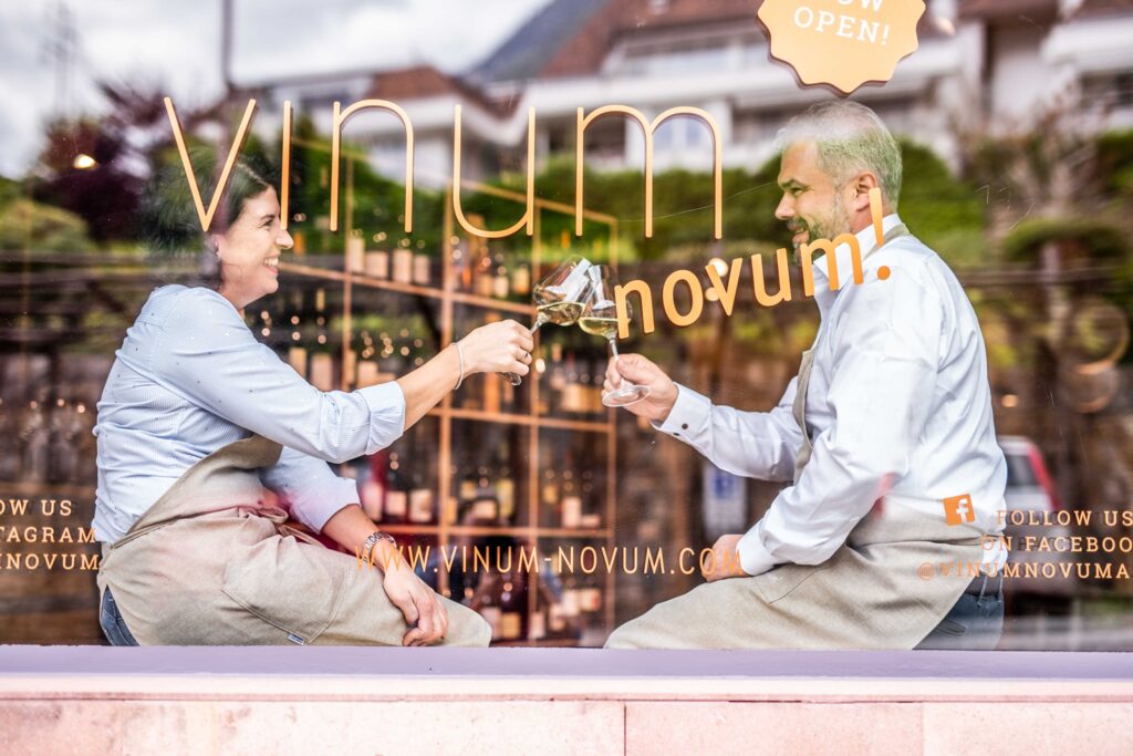 Man sieht einen Mann und eine Frau durch eine Glasscheibe mit der Aufschrift "Vinum Novum"