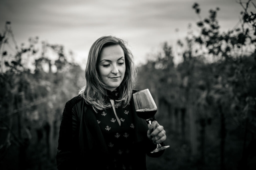 Eine junge Dame steht im Weinberg und hält ein Glas Wein in der Hand. Das Bild ist schwarz/weiß