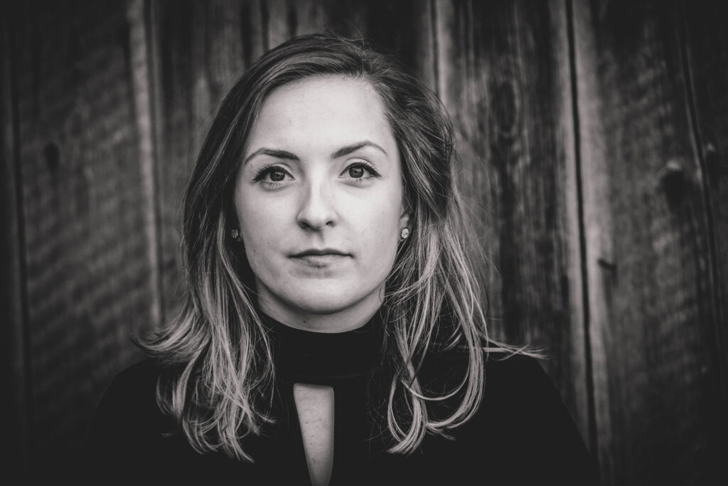 Ein schwarz/weiß portrait einer jungen Frau vor einer Holzwand