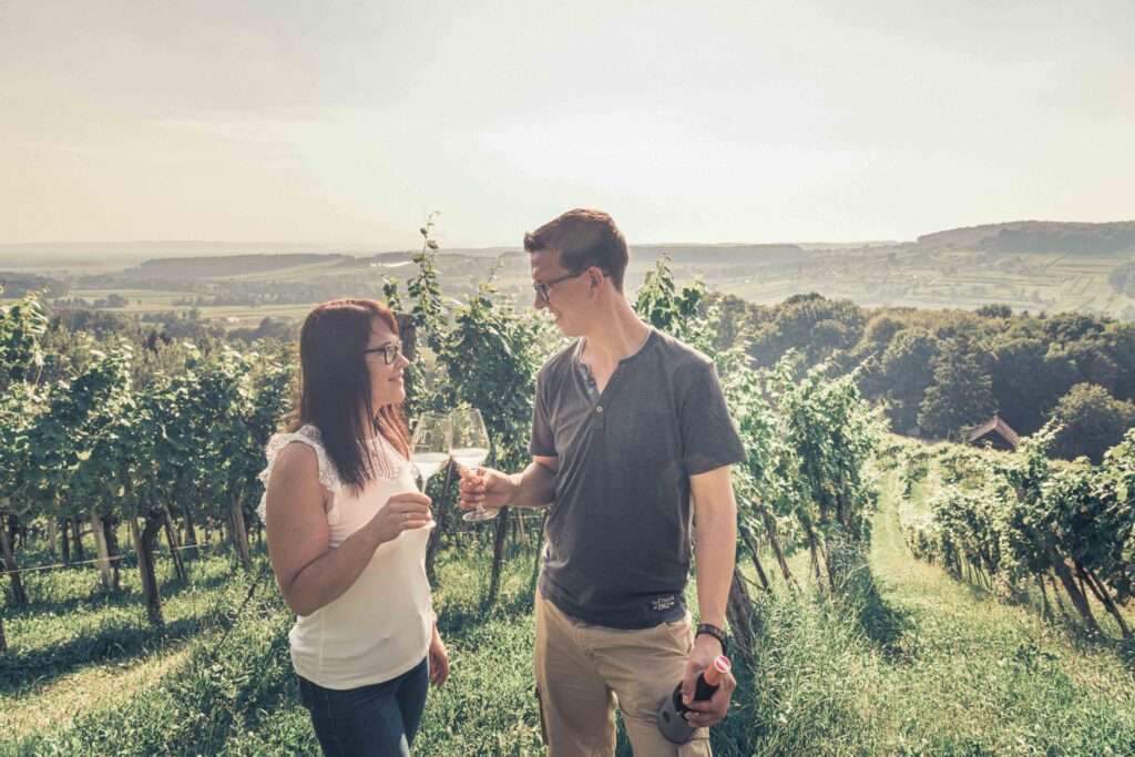 Mann und Frau stehen in einem Weinberg mit einem Glas Wein