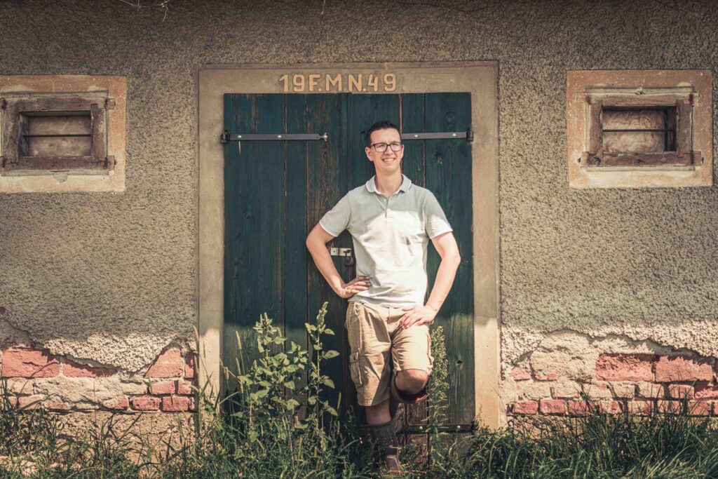 Werbefotografie- Porträtaufnahme eines jungen Winzers in Gummistiefeln an einer Holztür lehnend