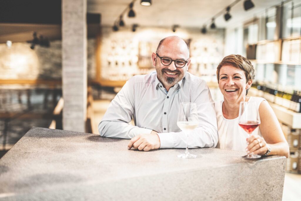 Portrait der Geschäftsführer vom Weingut Hiss ( Ein Mann, Eine Frau) an einer Theke lehnend.