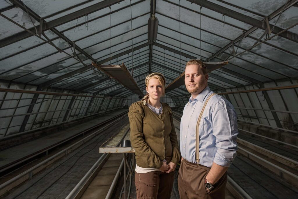 Mann und Frau stehen in ein Vintage- Mode gekleidet in einem Gewächshaus.