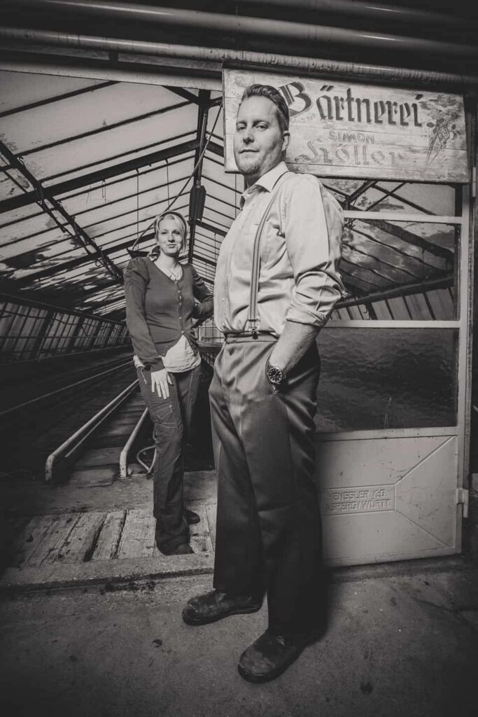 Mann und Frau stehen in ein Vintage- Mode gekleidet in einem Gewächshaus. Das Bild ist schwarz- weiß