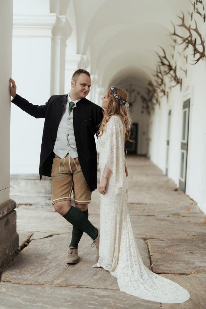 Hochzeitsfotografie - Portrtätaufnahme eines Brautpaares, an einer Säule lehnend in einem Gang, lachend