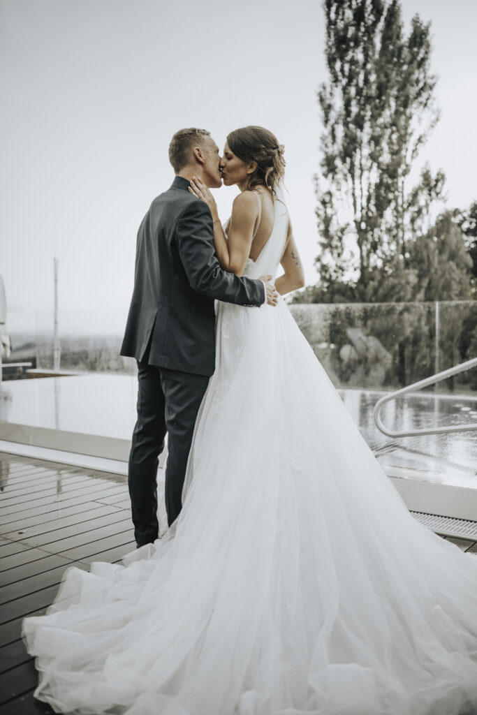 Hochzeitsfotografie- Porträtaufnahme eines küssenden Brautpaares neben einem Outdoor-SwimmingPool