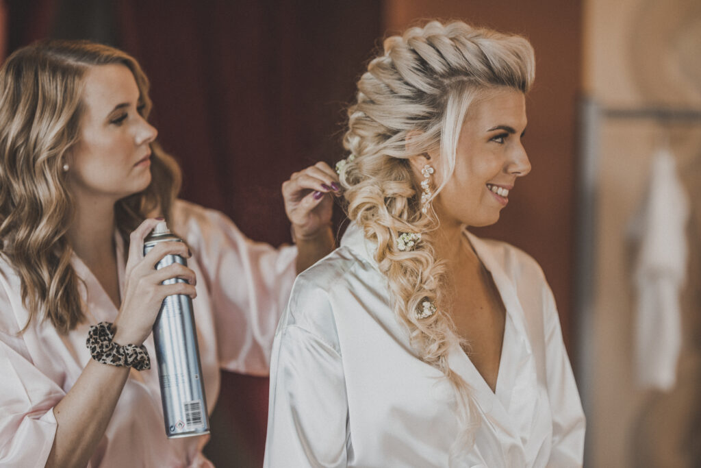 Hochzeitsfotografie- Frisörin arbeitet an den Haaren der Braut