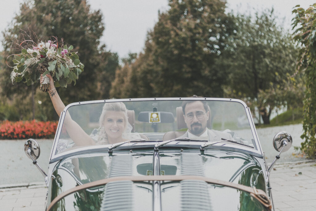 Hochzeitsfotografie - junges Brautpaar fährt in einem Oldtimer