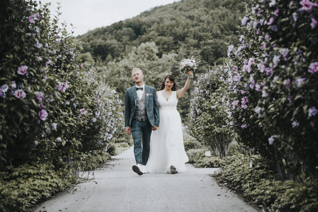 Hochzeitsfotografie- junges Brautpaar geht durch einen blühenden Garten