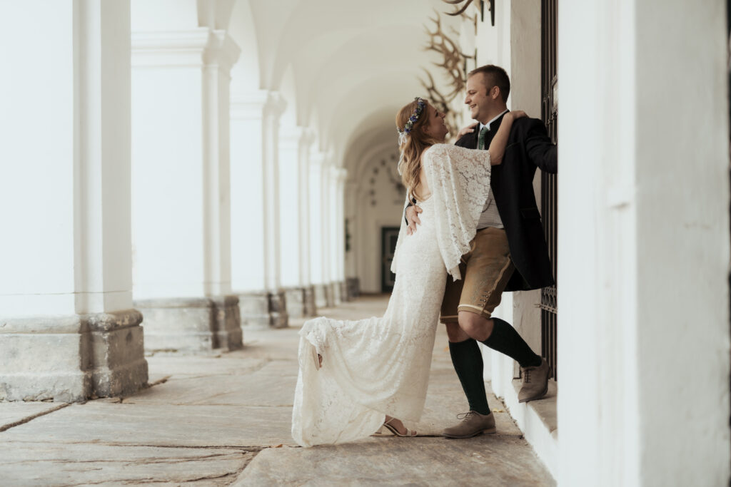 Hochzeitsfotografie - Portrtätaufnahme eines Brautpaares, an einer Säule lehnend in einem Gang, lachend