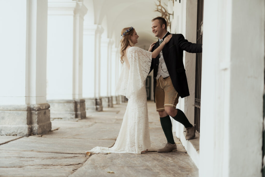 Hochzeitsfotografie - Portrtätaufnahme eines Brautpaares, an einer Säule lehnend in einem Gang, lachend