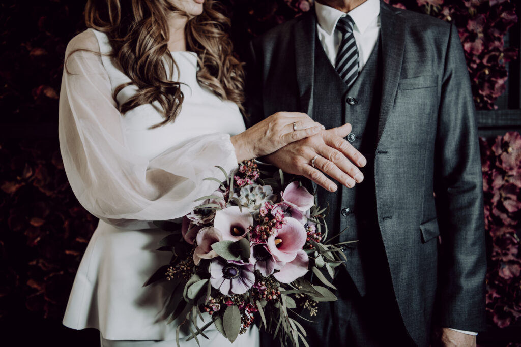 Hochzeitsfotografie- Porträt eines Brautpaares vor einer roten Blumenwand