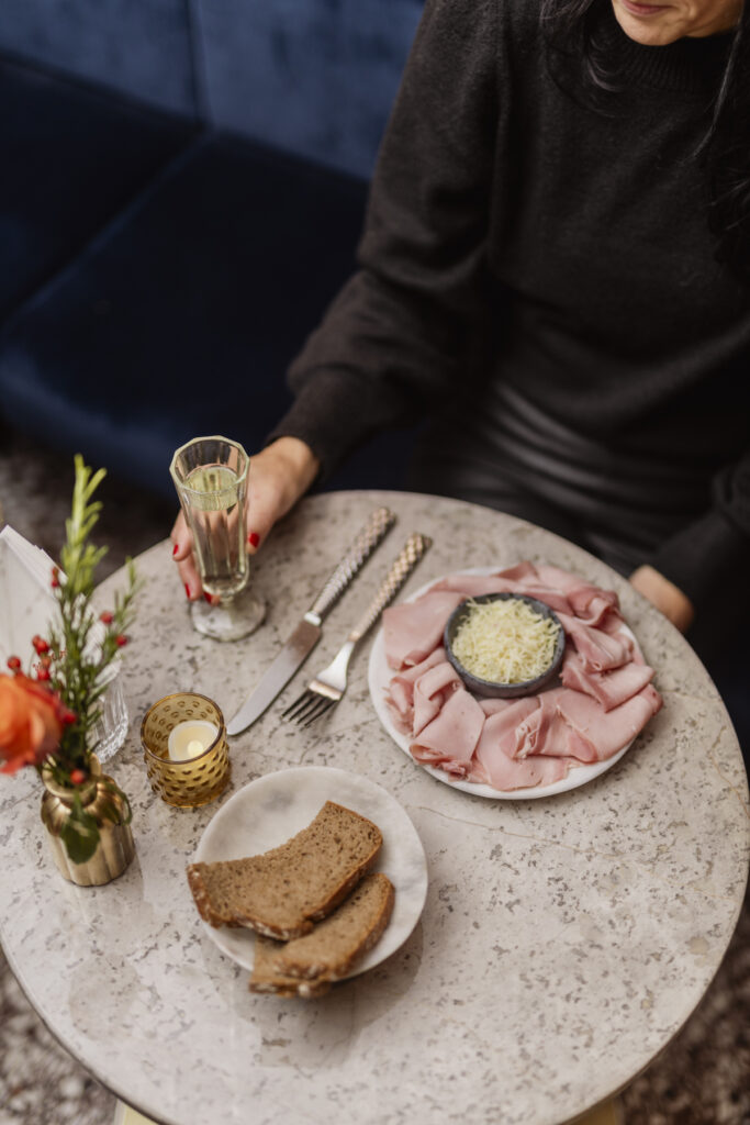 Werbefotografie/Foodfotografie- eine Frau sitzt am Tisch und greift zu einem Proseccoglas