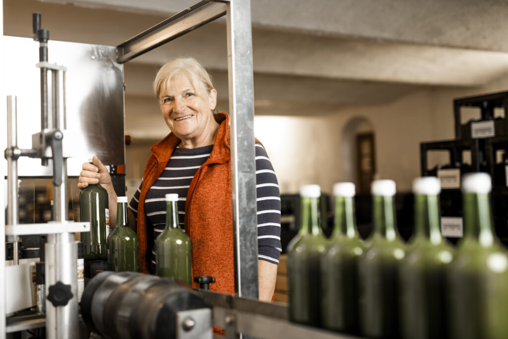 Werbefotografie- ältere Dame steht bei einer Abfüllanlage zwischen Flaschen